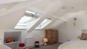 A bedroom with a sloped ceiling and skylights, a wooden dresser, a lamp, and a bed with a Union Jack pillow. - Upper Fernlea (Salcombe)