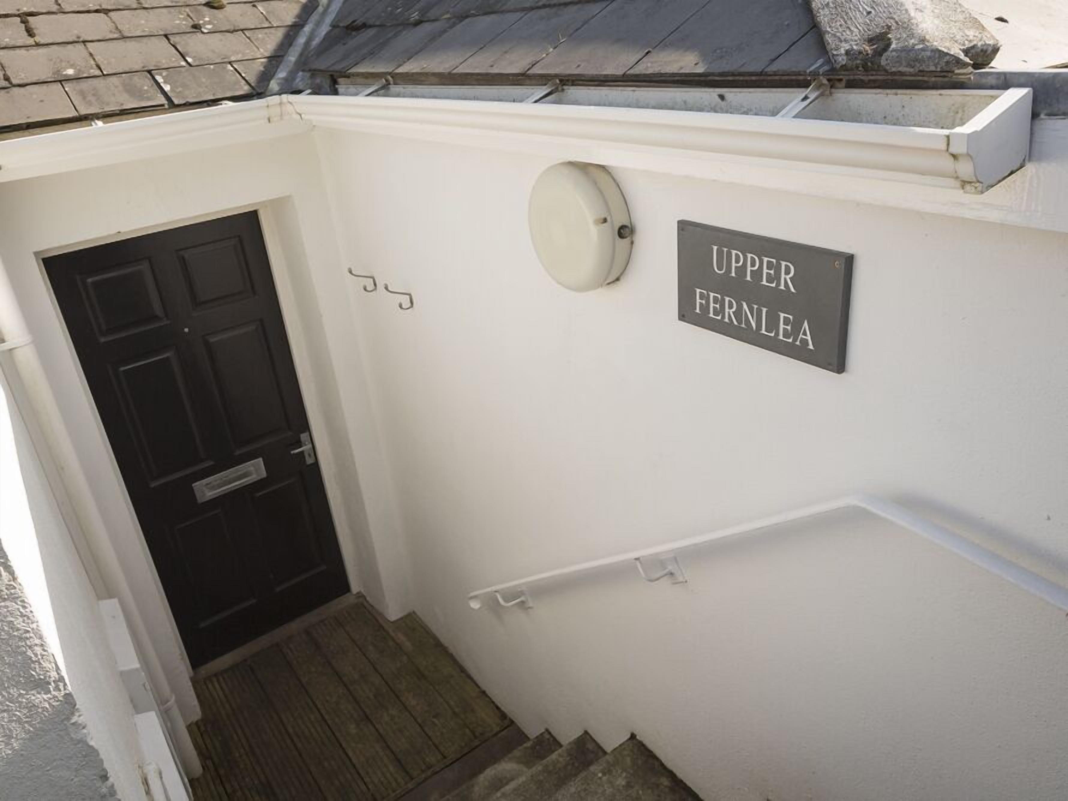 A white exterior wall with a black door and a sign reading "Upper Fernlea."