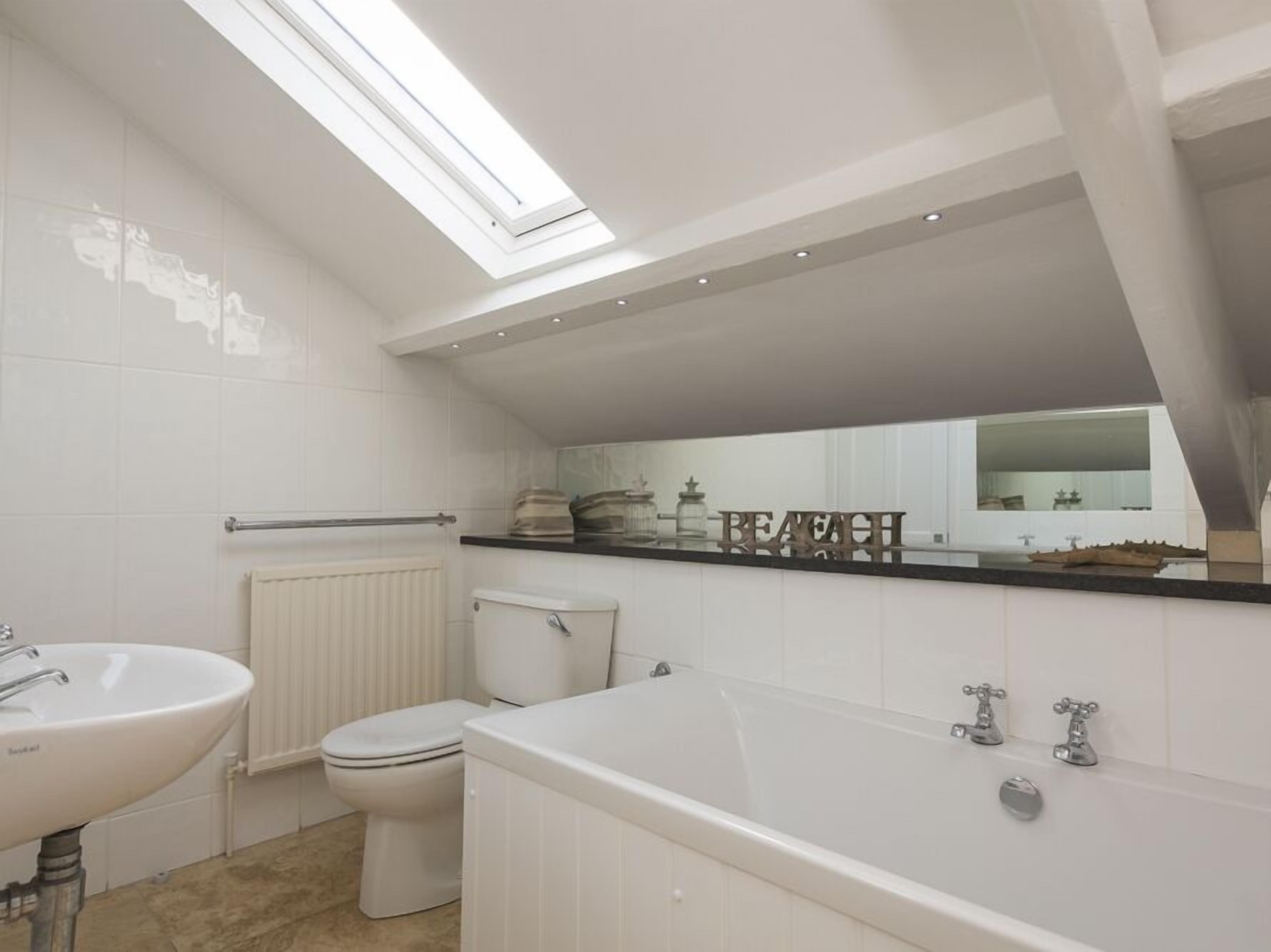 A modern bathroom with a skylight, a bathtub, a toilet, and a sink.