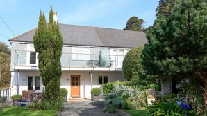 Une maison à deux étages avec une allée en gravier, une porte en bois et un petit jardin agrémenté de diverses plantes et d’un grand arbre.