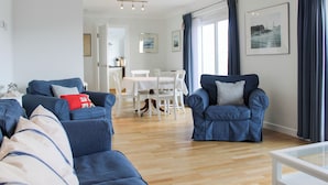 A modern living room with blue sofas, a dining table, and a kitchen in the background. - 2 Poundstone Court (Salcombe)