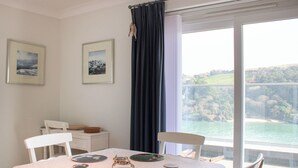 A dining area with a table set for four, two chairs, a white tablecloth, and a view of a lake through a large window. - 2 Poundstone Court (Salcombe)