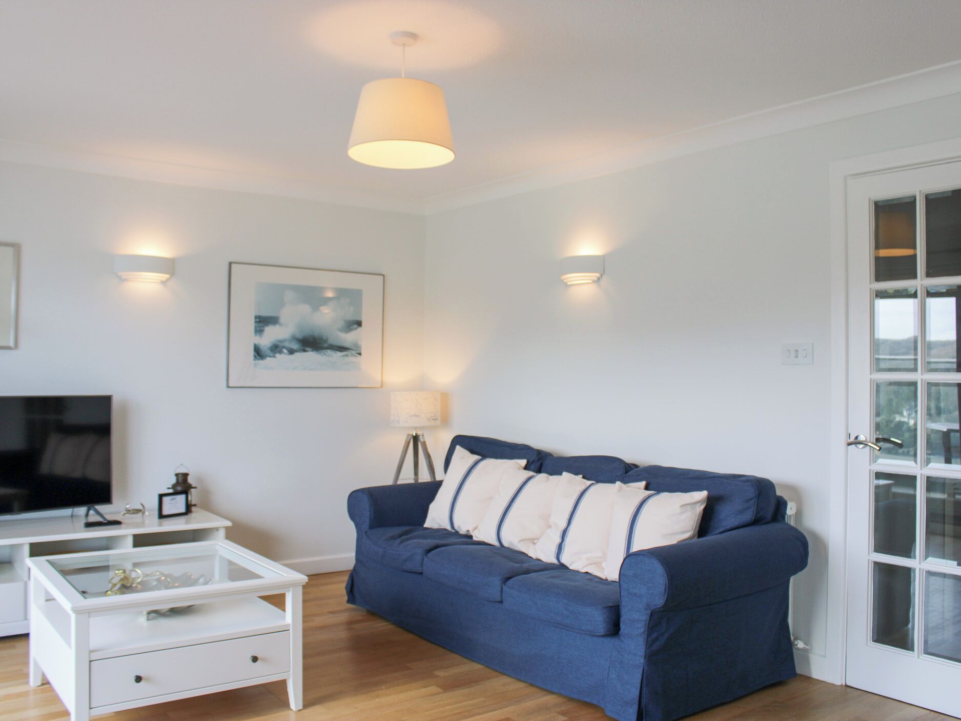 Ein Wohnzimmer mit blauem Sofa, einem Glastisch, einem Fernseher und einer Glastür.