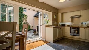 A modern kitchen with a dining area, large windows, and a view of greenery outside. - Mill Race (Burford)