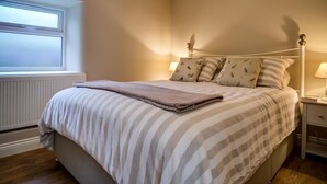 A bedroom with a bed, a nightstand, a window, and a radiator. - Mill Race (Burford)