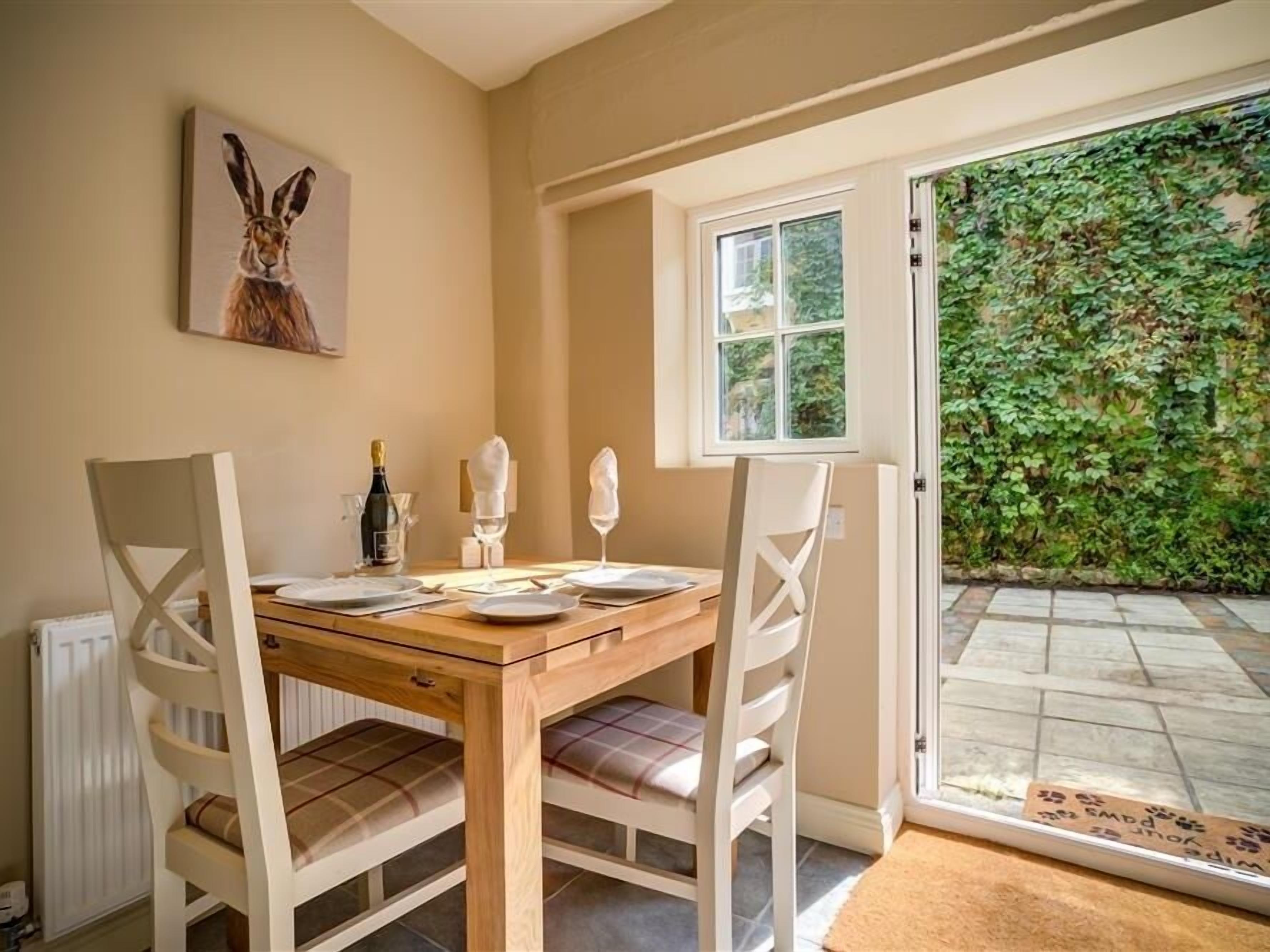Un comedor con una mesa de madera, sillas blancas y un aparador de vidrio.