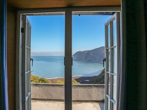A view through a glass door of a coastal landscape with a clear sky, a body of water, and a distant mountain range. - C S Lewis Balcony (Lynton)