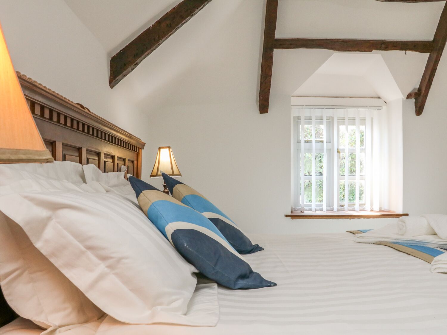 Ein Schlafzimmer mit einem Bett, Kissen, einer Lampe und einem Fenster mit Vorhängen.