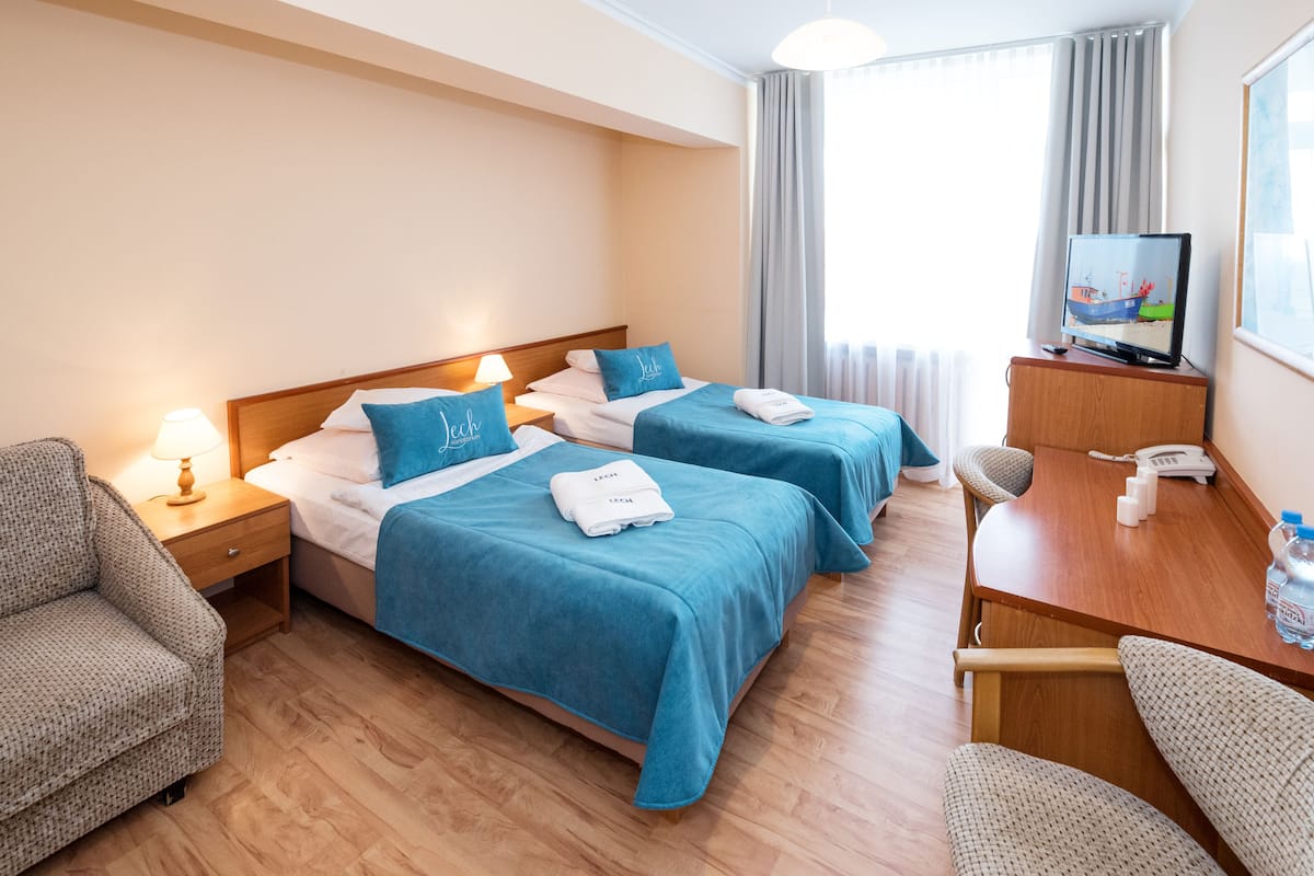 A hotel room with two beds, a desk, a TV, and a chair.