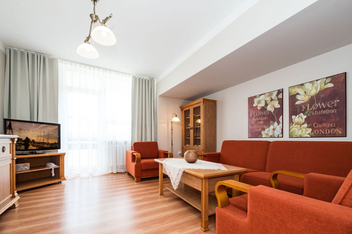 A living room with a television, red sofa, wooden cabinet, and floral wall art.