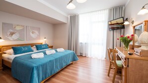 A hotel room with a bed, a desk, a chair, a TV, and a window with curtains. - Lech Sanatorium Uzdrowiskowe (Kolobrzeg)