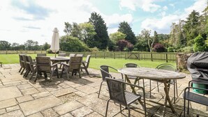 An outdoor patio with a round table and chairs, surrounded by a stone floor. - Home Farm (Witney)