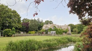 A traditional stone house with a conservatory, surrounded by a well-maintained lawn and a small pond. - Home Farm (Witney)