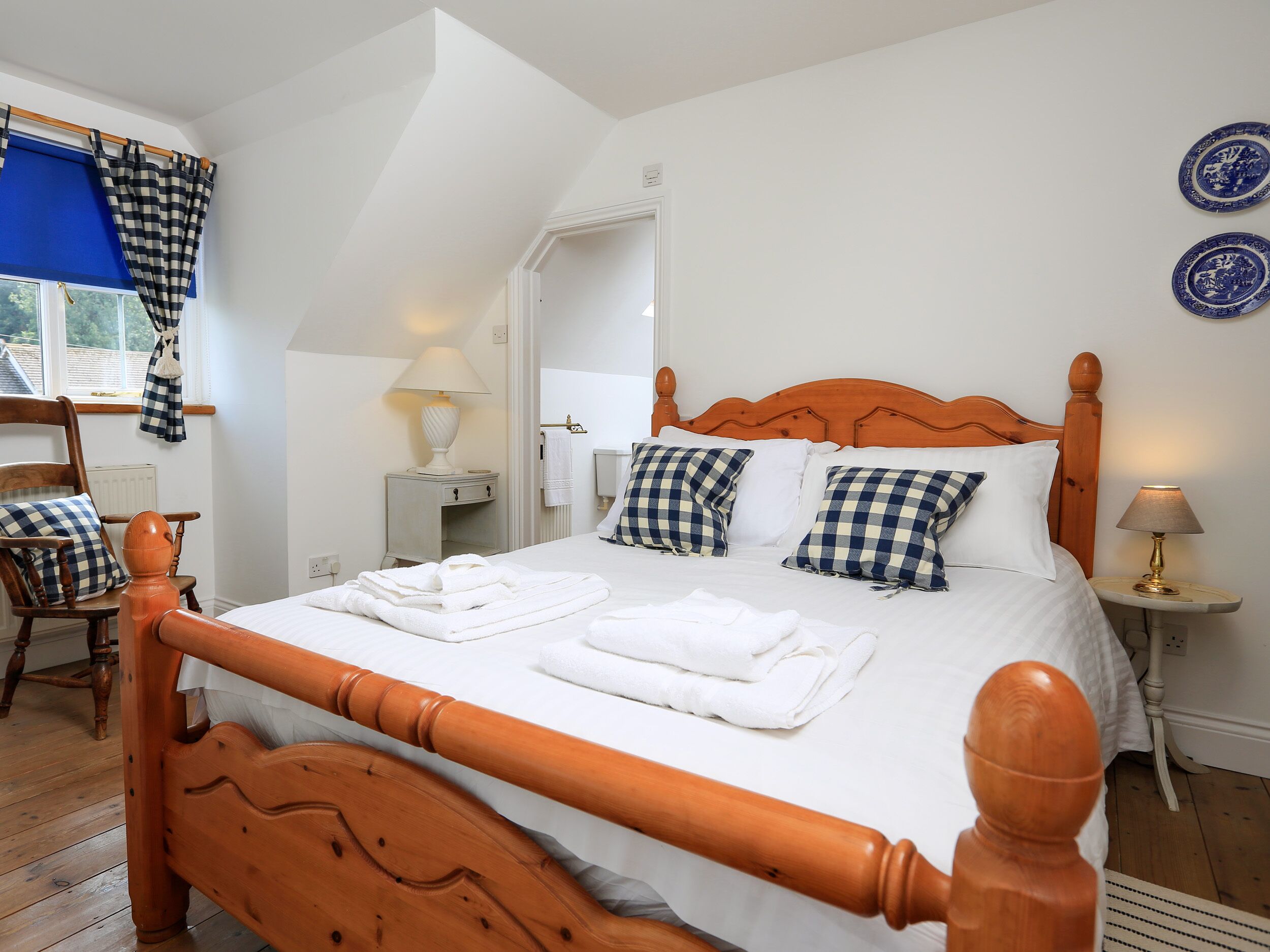 A neatly made bed with checkered pillows, a wooden headboard, and a bedside table with a lamp.