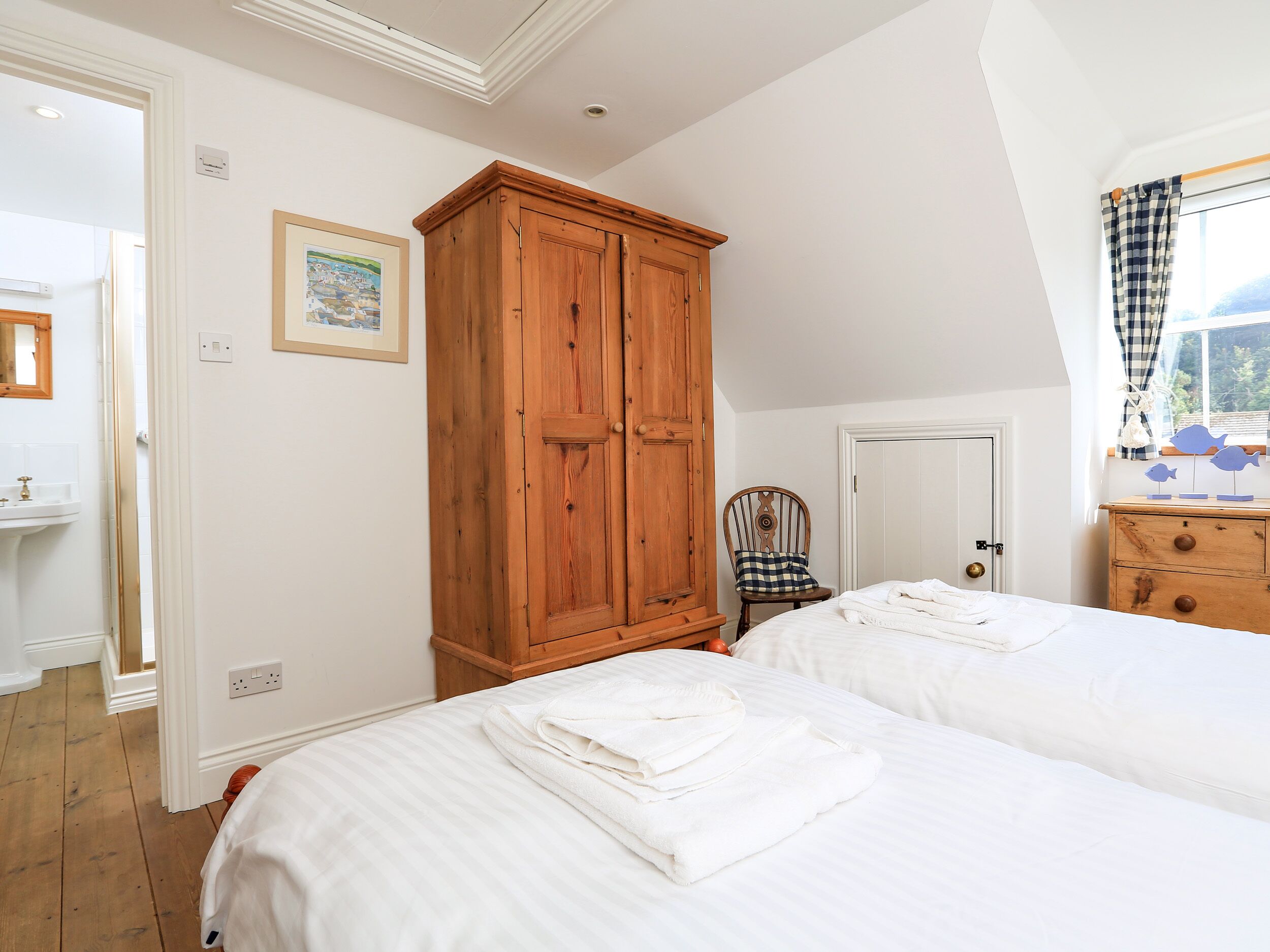 A bedroom with two beds, a wooden wardrobe, a chair, and a window with curtains.