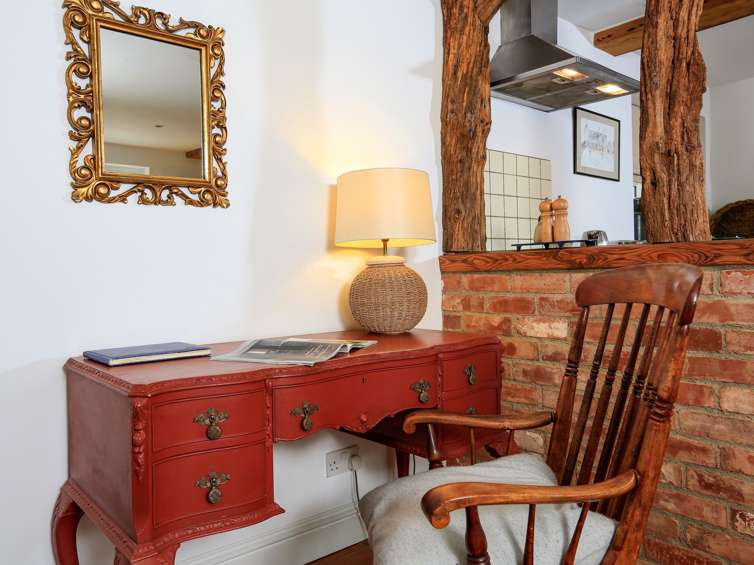 Un escritorio de madera rojo con cajones, una lámpara y una silla.