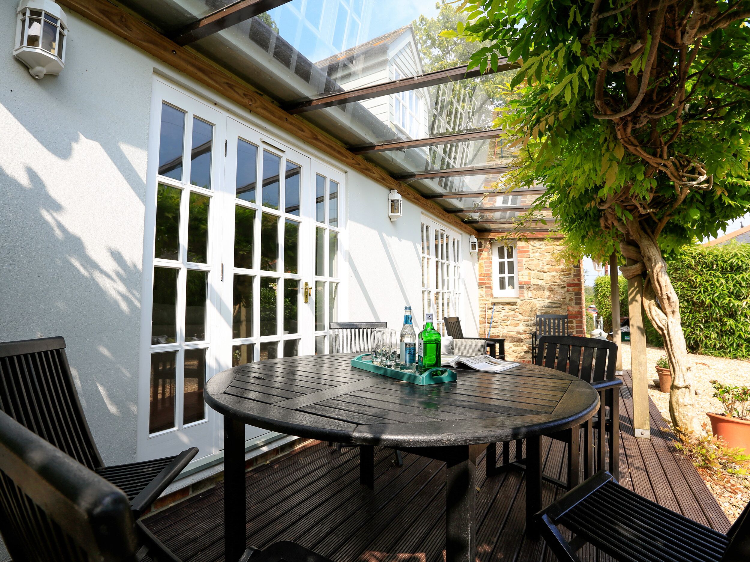 Eine überdachte Terrasse im Freien mit einem runden Tisch und Stühlen, einer Steinwand und einem Baum.