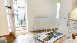 A bright kitchen with a wooden table, a yellow chair, a white radiator, and a view of the outside. - The Hayloft (Hawes)