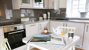 A modern kitchen with white cabinetry, a Bosch oven, a sink, and a dining area with a table and chairs. - The Hayloft (Hawes)