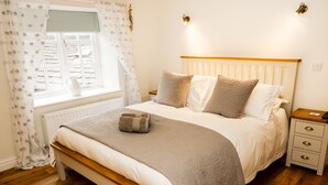 A bedroom with a wooden bed, white bedding, a bedside table, and a nightstand. - The Hayloft (Hawes)
