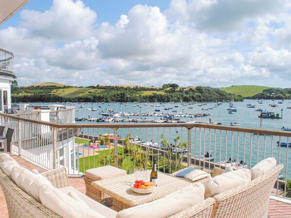 A balcony with wicker furniture, a table with a bottle and glasses, and a view of a marina with boats.