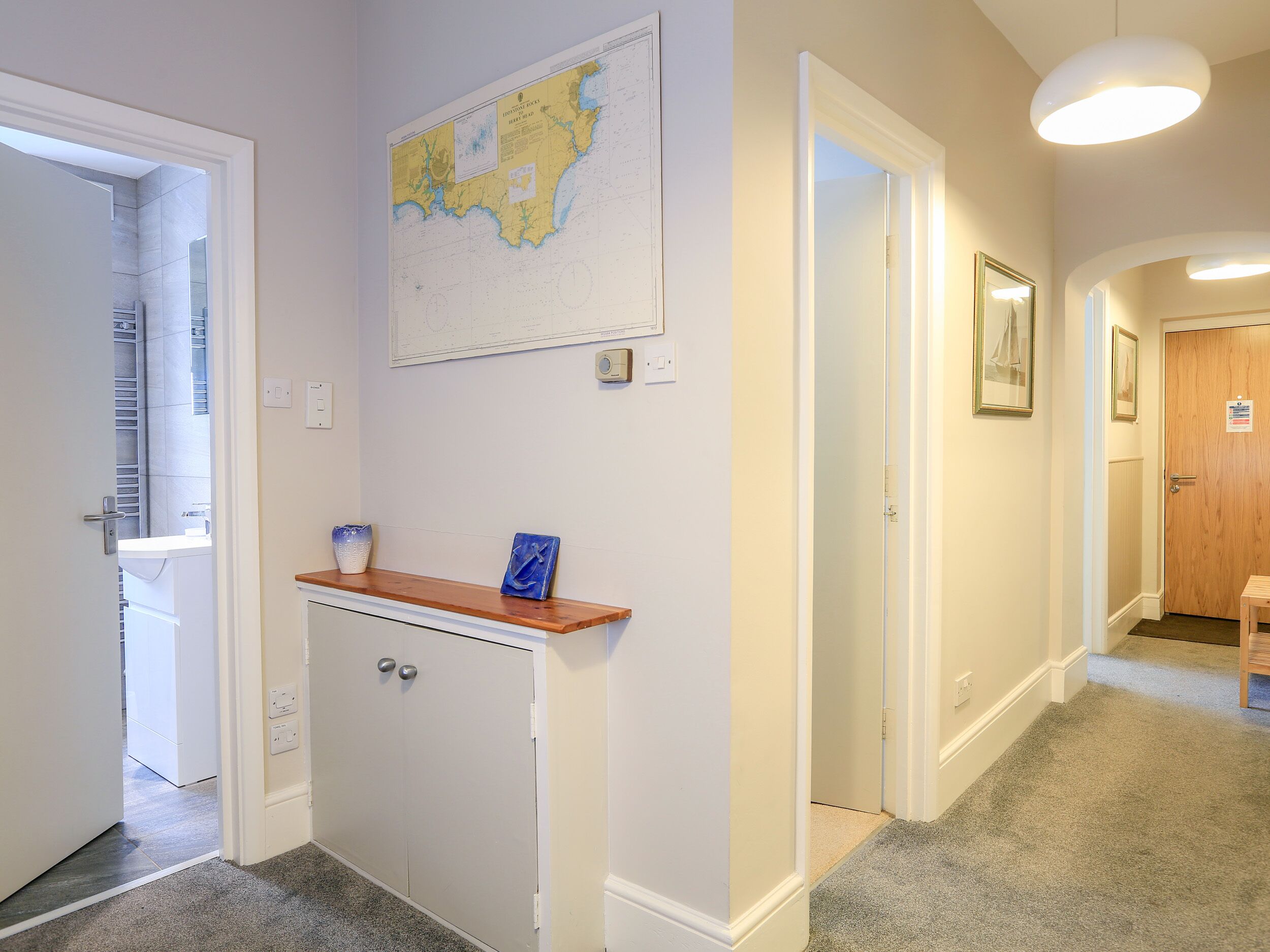A hallway with a map on the wall, a small cabinet with a vase, and a wooden door.