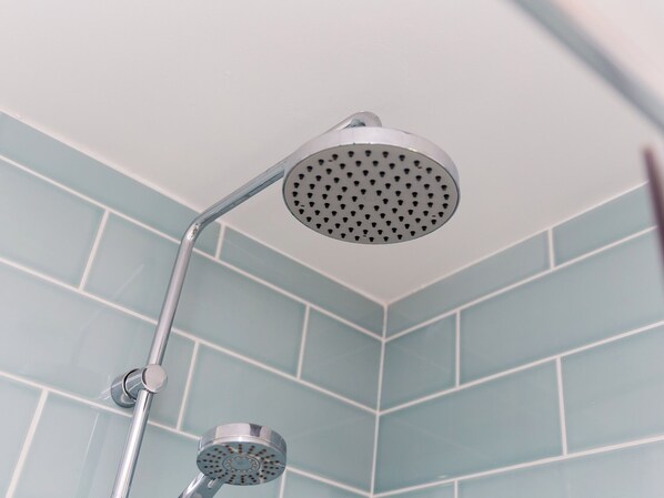 A corner of a bathroom with light blue tiles and a chrome showerhead.