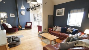 A cozy living room with a wooden floor, a leather sofa, a red armchair, and a coffee table. - Horseshoe Cottage (Pwllheli)