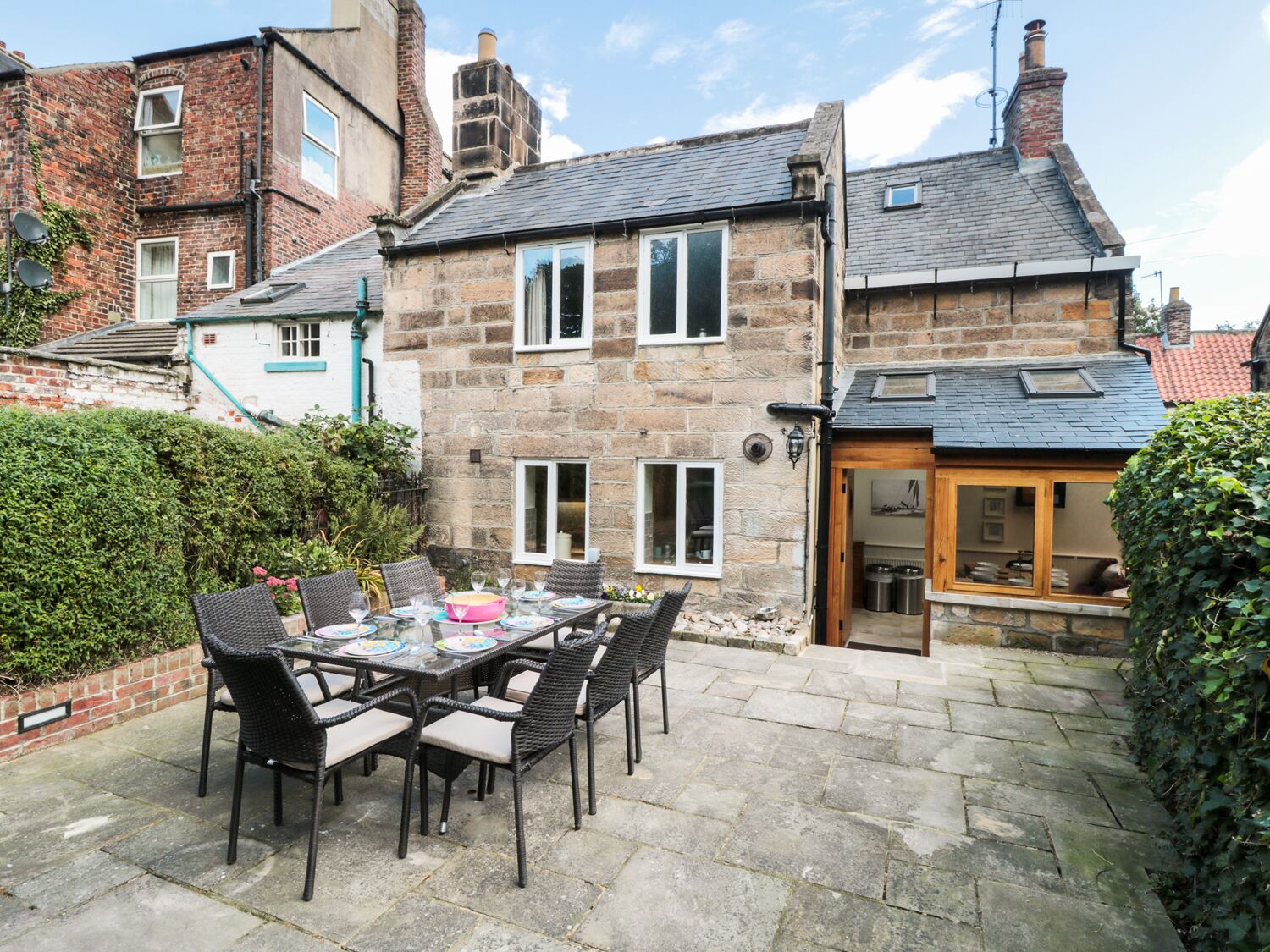 A stone house with a patio table and chairs, a wooden door, and a small garden.