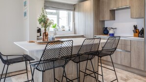 A modern kitchen with a central island, bar stools, and wooden cabinets.