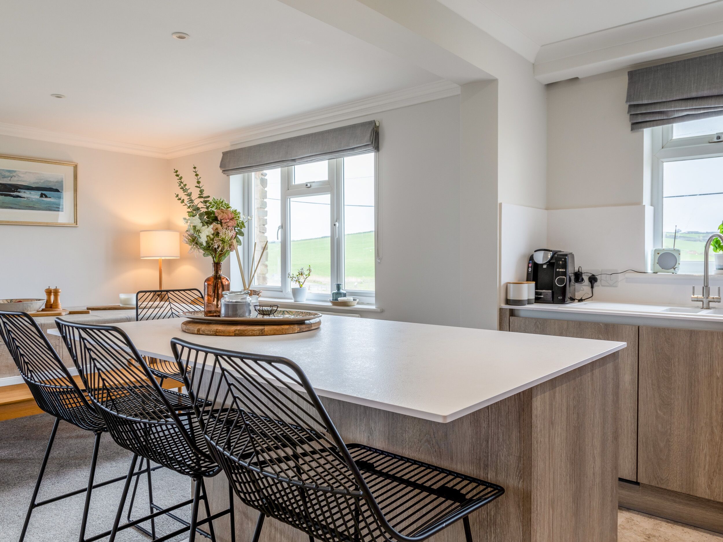 Una cocina moderna con una isla central, sillas de malla metálica negra, una mesa de comedor y vistas al exterior.