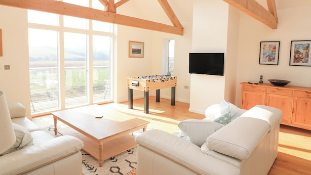 A spacious living room with a high ceiling, a foosball table, a sofa, a coffee table, and a television mounted on the wall. - Sea Peep (Kingsbridge)