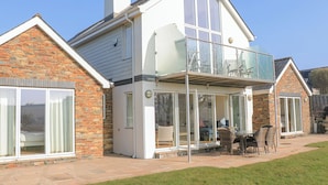 A two-story house with a balcony, large windows, and a patio area with outdoor furniture. - Sea Peep (Kingsbridge)