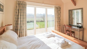 A bedroom with a large bed, a desk, and a chair. There is a view of a green landscape through the window. - Sea Peep (Kingsbridge)