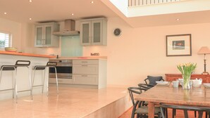 A modern kitchen with a dining area, featuring a kitchen island, bar stools, and a dining table with chairs. - Sea Peep (Kingsbridge)
