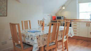Un coin repas avec une table dressée pour six personnes, des chaises en bois, une carte accrochée au mur et une cuisine en arrière-plan.