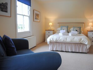 A bedroom with a bed, bedside tables, a window, a radiator, and a blue sofa. - 7 Glenthorne House (Salcombe)