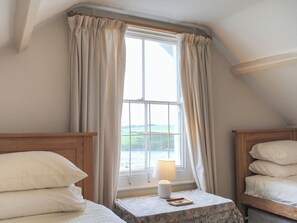 Une chambre avec deux lits simples, une fenêtre avec des rideaux, une table de chevet avec une lampe et une vue sur l’extérieur.