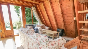 Ein gemütlicher Raum mit holzgetäfelter Schräge, einer Sofagarnitur, einem kleinen Tisch und einem Heizgerät.