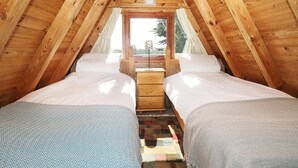 Ein gemütliches Schlafzimmer im Dachgeschoss mit zwei Betten, Holzbalken und einem Fenster mit Blick ins Grüne.