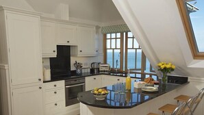 A kitchen with white cabinets, a black countertop, and a view of the sea through large windows. - 9 Prospect House (Kingsbridge)