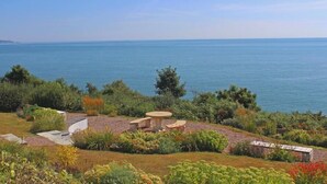 A coastal landscape with a garden area featuring a stone table and a small stone structure, overlooking the sea. - 9 Prospect House (Kingsbridge)