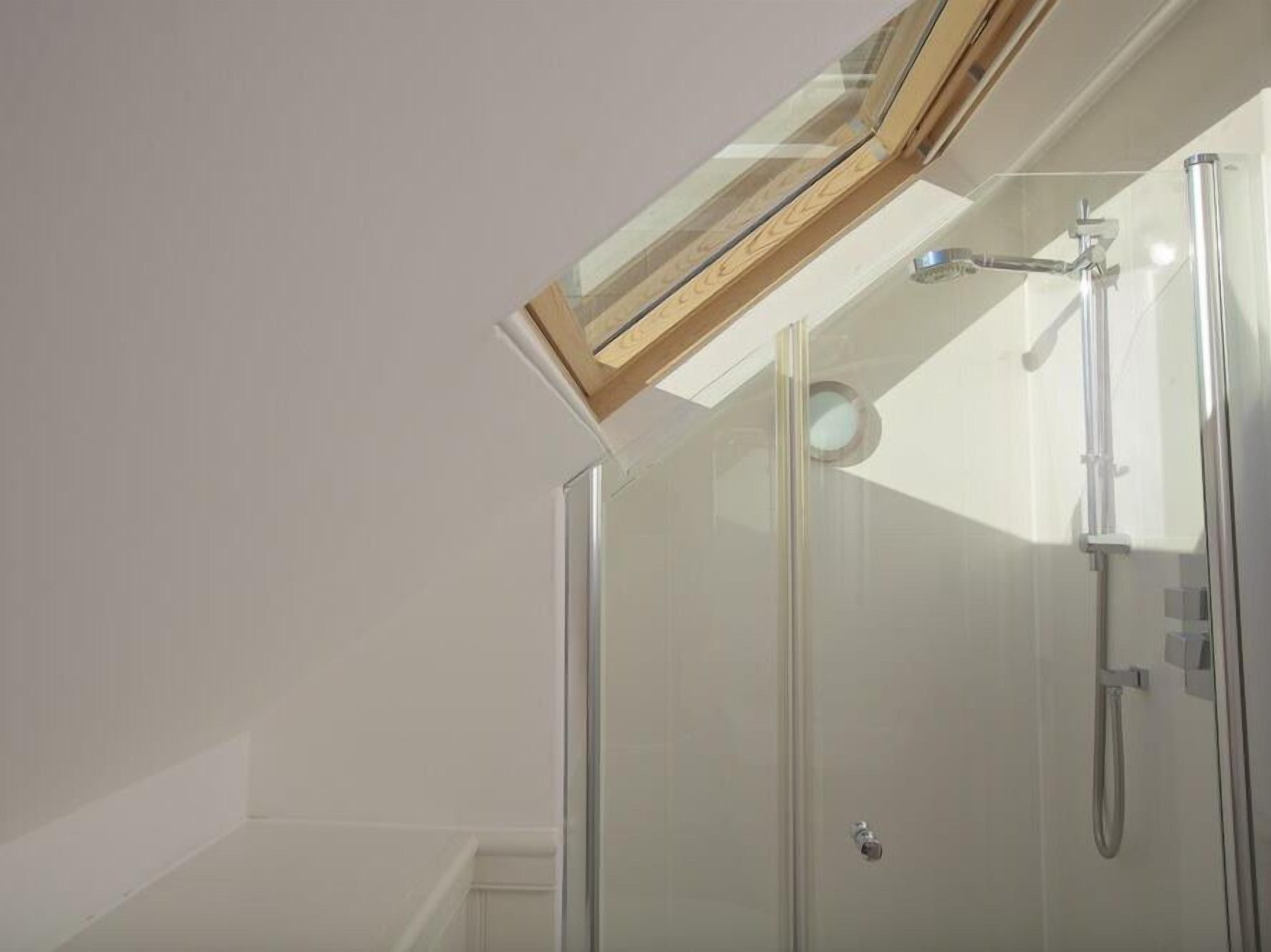 A glass-enclosed shower with a skylight above, a visible shower head, and a door handle.