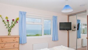Un dormitorio con cama, cómoda, televisor y ventana con cortinas.