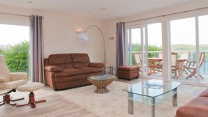 Un salón amplio con un sofá marrón, una mesa de centro de vidrio y vistas a un balcón con mobiliario exterior.