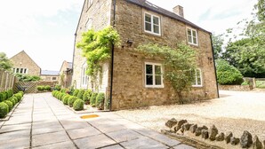 A stone building with a paved pathway leading to it, surrounded by well-maintained hedges and a gravel area. - South Hill Farmhouse (Cheltenham)
