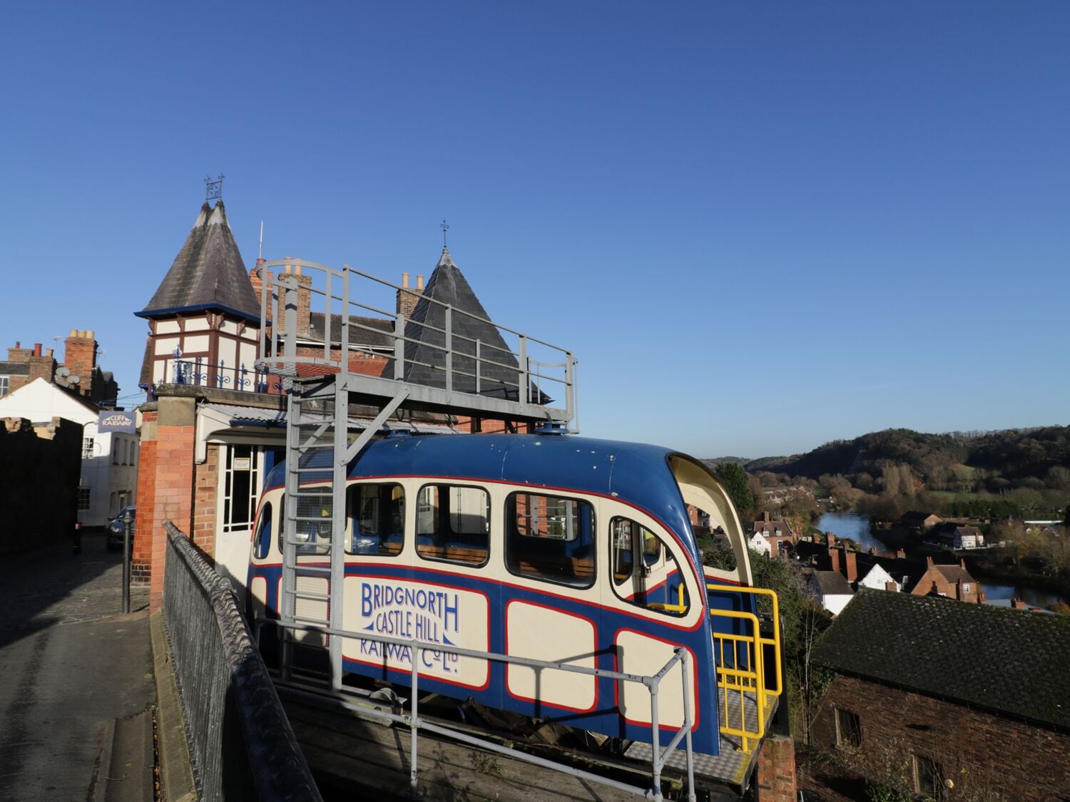 A double-decker train with "Bridgnorth Castle Hill Railway Co." written on the side, parked on a track with a bridge overhead.