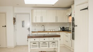 Una cuina moderna amb armaris blancs, una illa central amb calaixos, un fanal i forn integrat.