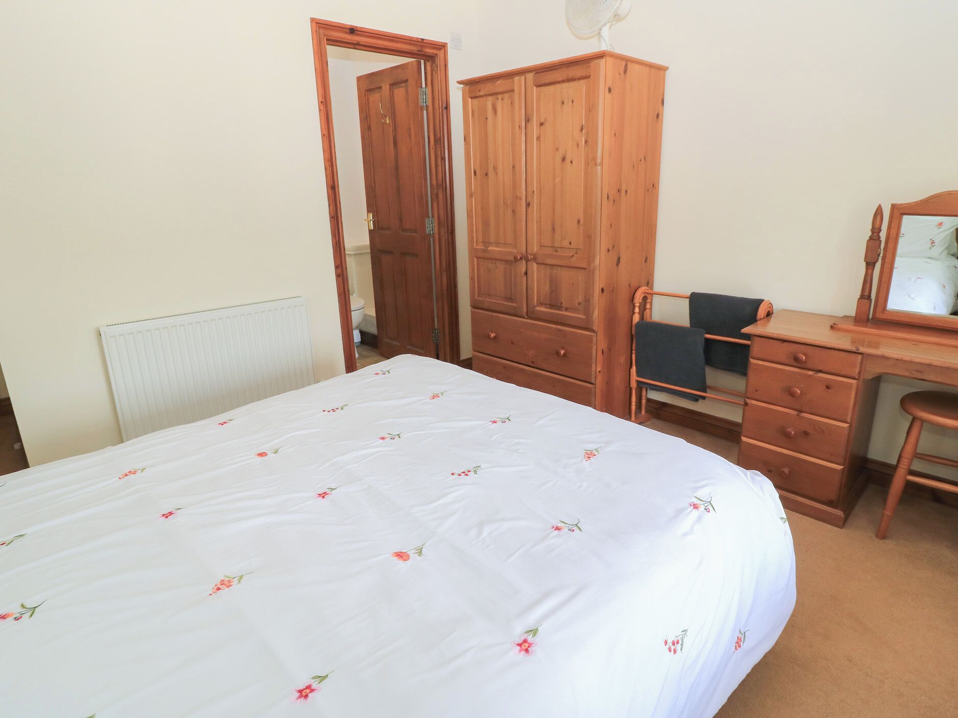 Une chambre à coucher avec un lit, une armoire en bois, un bureau avec une chaise et un miroir.