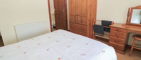 Une chambre à coucher avec un lit, une armoire en bois, un bureau avec une chaise et un miroir.